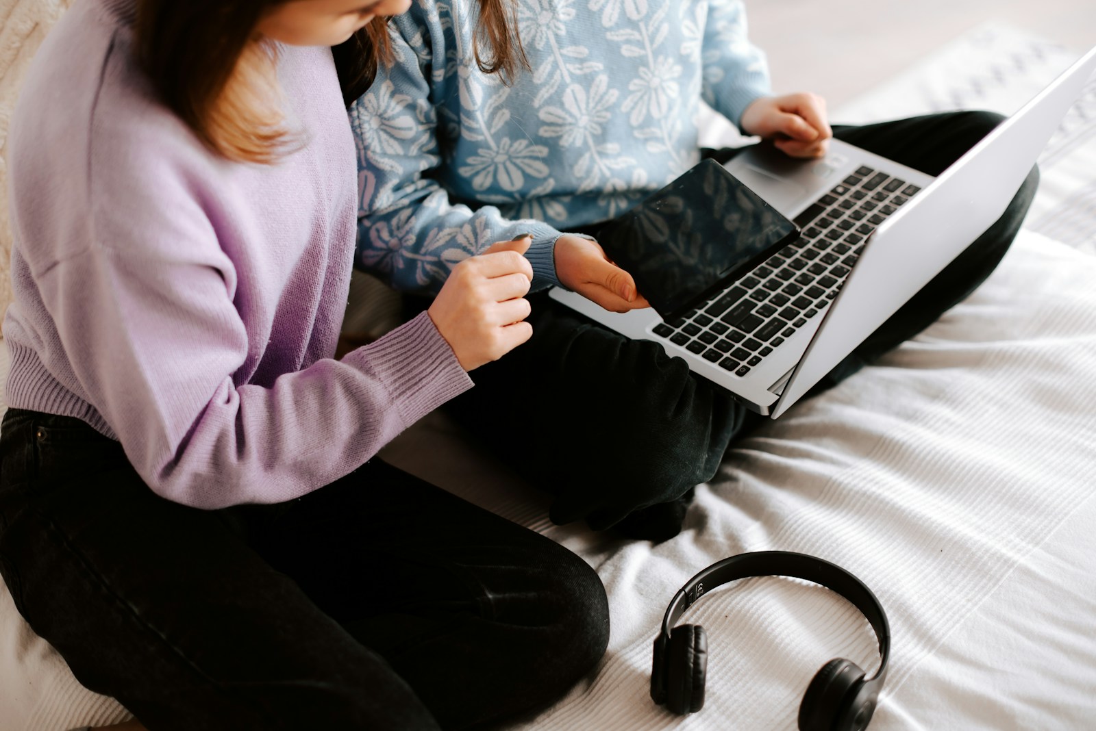 two girls sitting on a bed with a laptop and headphones